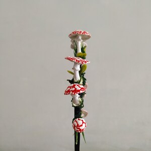 May include: A red and white mushroom garland with green leaves and a black wire stem.