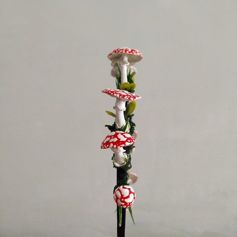 May include: A red and white mushroom garland with green leaves and a black wire stem.