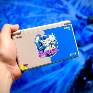 May include: A Nintendo Game Boy Advance SP handheld console with a custom design. The top half is beige, and the bottom half is blue with a Pokemon graphic. The graphic includes the text "Pokemon" in Japanese.
