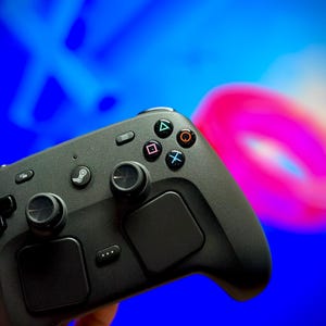 Op de afbeelding: Een matzwarte draadloze gamecontroller met twee analoge sticks, een richtingspad, twee grote trackpads en vier actieknoppen gemarkeerd met driehoek-, vierkant-, kruis- en cirkelsymbolen. Een centrale Steam-logoknop is duidelijk zichtbaar.