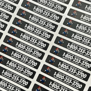 K&ouml;nnte beinhalten: Eine Reihe von schwarz-wei&szlig;en Aufklebern mit einer Comicfigur, die einen Schraubenschl&uuml;ssel h&auml;lt. Die Aufkleber zeigen den Text "Installation, Wartung oder Service" und die Telefonnummer "1-800-255-3700". Der Text "Nintendo World Class Service, Center Hotline" ist ebenfalls auf den Aufklebern enthalten.