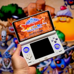May include: A white Nintendo 3DS handheld game console displaying the "Dragon Quest VIII" game. The screen shows the game's title in red and gold. The console has blue-lit buttons and is held in a hand against a background of game characters.