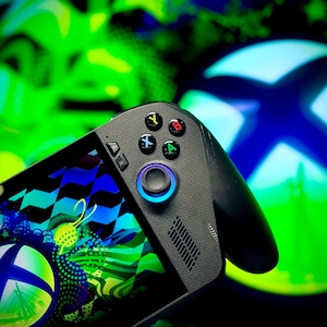 Peut inclure: Une manette de jeu portable noire et grise avec des boutons colorés et un joystick éclairé en bleu. La manette présente un motif avec des accents bleus, verts et blancs. L'arrière-plan présente un logo Xbox vert et bleu.