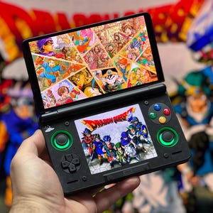 Può includere: Console di gioco portatile nera con due schermi che mostrano opere d'arte colorate di Dragon Quest. Lo schermo inferiore mostra il titolo del gioco e i personaggi. La console ha pulsanti verdi e colorati.
