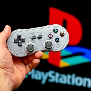 Peut inclure: Une manette 8BitDo SN30 Pro blanche avec des boutons noirs et un logo PlayStation en arrière-plan.