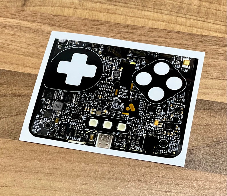 May include: A black and white circuit board with a white plus sign and four white circles. The board has text that reads "P/N: 6513C V0.06 060921".