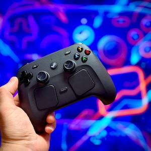 Peut inclure: Une manette de jeu vidéo sans fil noire dotée de deux joysticks analogiques, d'une croix directionnelle, de quatre boutons d'action colorés marqués A, B, X et Y, de deux grands pavés tactiles et d'un bouton central avec le logo Steam.