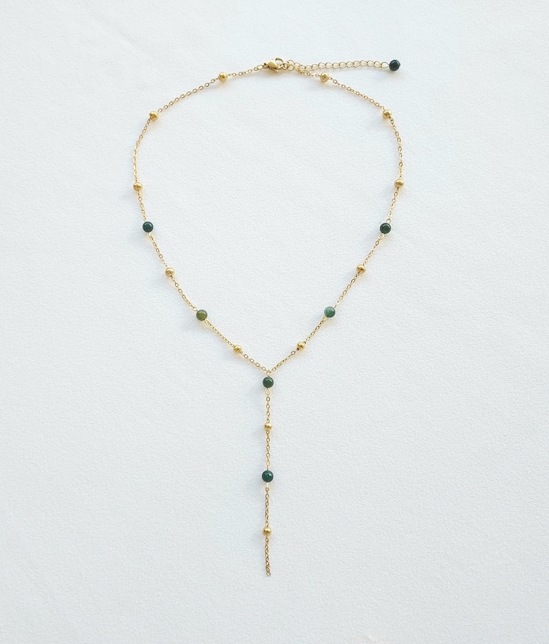 May include: A gold chain necklace with green gemstone beads. The necklace has a Y-shaped design with a longer strand extending from the center.