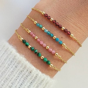 Peut inclure: Quatre bracelets en chaîne dorée avec des perles de pierres précieuses de différentes couleurs. Les bracelets présentent des perles vertes, roses, bleues et rouges.