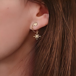 May include: Gold star-shaped earring with a small chain and a round charm hanging from the earlobe.