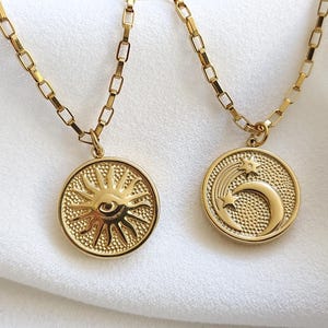 Peut inclure: Deux colliers en or avec des pendentifs. Un pendentif représente un soleil avec un œil au centre. L'autre pendentif représente une lune croissante avec une étoile et une étoile filante.