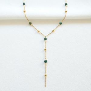 May include: A gold chain necklace with green gemstone beads. The necklace has a Y-shaped design with a longer strand extending from the center.