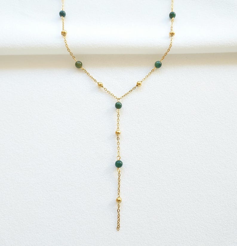 May include: A gold chain necklace with green gemstone beads. The necklace has a Y-shaped design with a longer strand extending from the center.