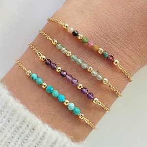 Op de afbeelding: Vier gouden kettingarmbanden met verschillende gekleurde edelsteen kralen. De armbanden hebben turquoise, amethyst, aquamarijn en roze en groene toermalijn kralen.