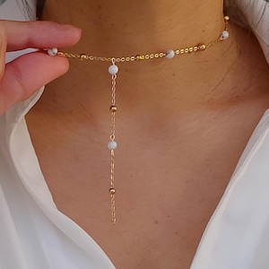 May include: A gold chain necklace with white beads. The necklace has a long, dangling chain with white beads.