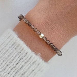 Peut inclure: Un bracelet en pierres précieuses brunes avec un accent de perle argentée. Le bracelet est composé de petites perles rondes et est porté au poignet.