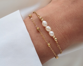 May include: A gold chain bracelet with small round beads and a row of white pearls.