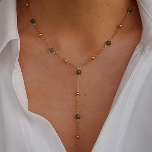 May include: A gold chain necklace with green gemstone beads. The necklace has a Y-shaped design with a longer strand extending from the center.
