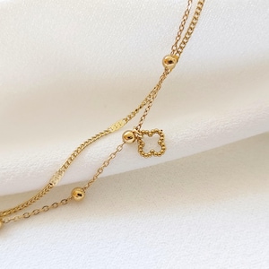May include: A gold chain anklet with a small clover charm. The chain is made of two strands of different sizes.