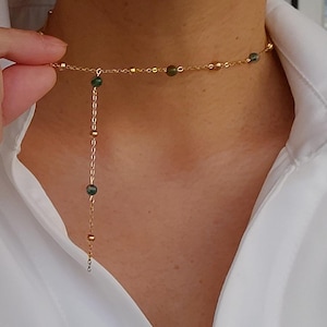 May include: A gold chain necklace with a delicate pendant featuring small green beads. The necklace is layered with a shorter chain that sits closer to the neck.
