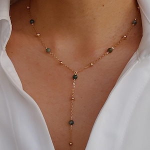 May include: A gold chain necklace with green gemstone beads. The necklace has a Y-shaped design with a longer strand extending from the center.
