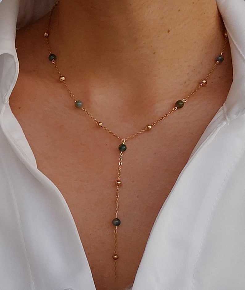 May include: A gold chain necklace with green gemstone beads. The necklace has a Y-shaped design with a longer strand extending from the center.