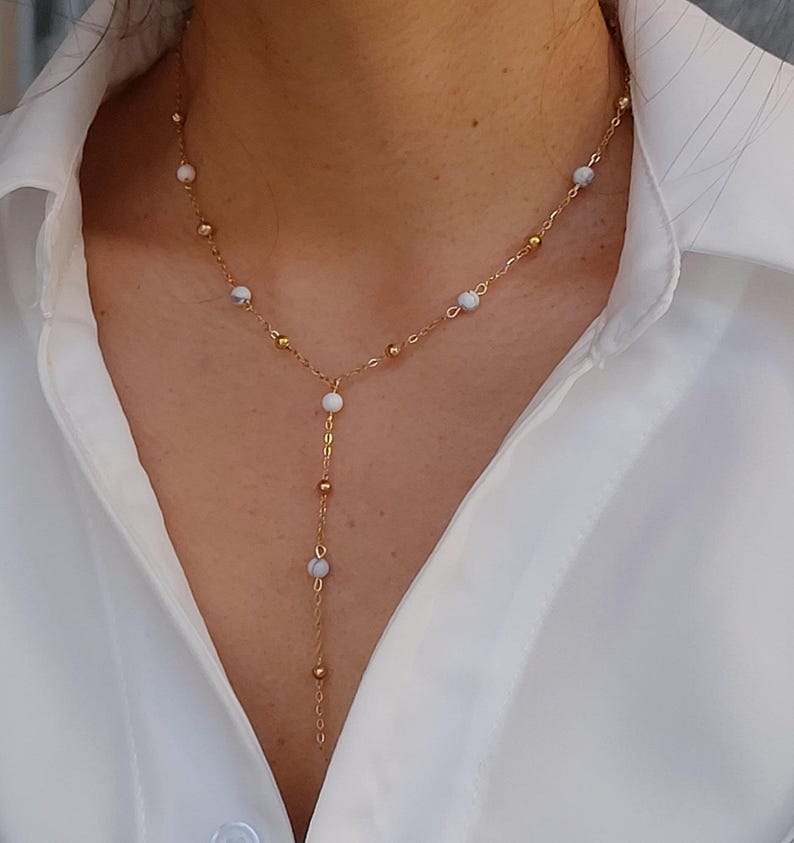 May include: A gold chain necklace with white beads and a long pendant. The necklace is layered and features small gold beads.