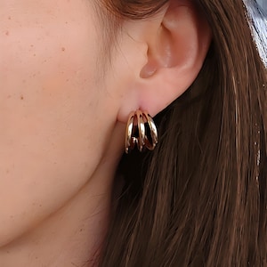 Peut inclure: Boucles d'oreilles créoles dorées avec plusieurs anneaux. Les boucles d'oreilles sont d'un design simple et élégant.