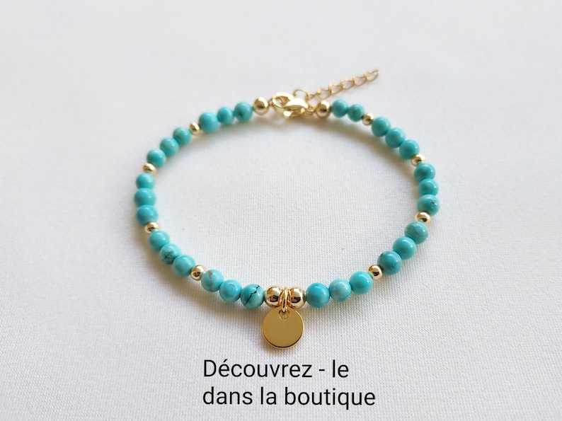 K&ouml;nnte beinhalten: T&uuml;rkisfarbenes Perlenarmband mit goldfarbenen Akzenten und einem kleinen, runden Anh&auml;nger. Das Armband hat kleine, runde t&uuml;rkisfarbene Perlen und goldfarbene Perlen. Der Verschluss und der Anh&auml;nger sind ebenfalls goldfarben. Der Text "D&eacute;couvrez - le dans la boutique" steht unten.