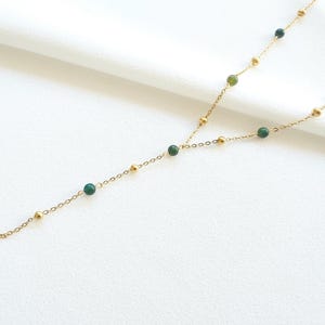 May include: A gold chain necklace with green gemstone beads. The necklace is long and has a Y-shaped design.