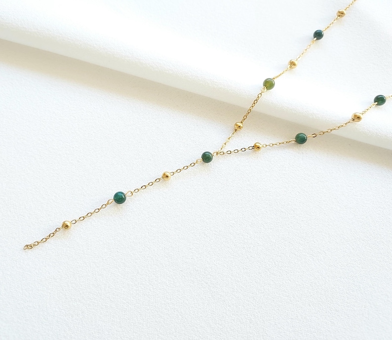 May include: A gold chain necklace with green gemstone beads. The necklace is long and has a Y-shaped design.