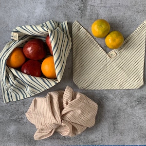 May include: Three striped fabric bags, two with blue and white stripes and one with pink and white stripes. The blue and white bags are filled with oranges and apples. The pink and white bag is folded and empty.