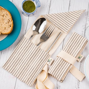 Puede incluir: Un juego de dos cubiertos reutilizables, cada uno con un tenedor, un cuchillo y una cuchara, envueltos en una bolsa de tela a rayas. Las bolsas están hechas de tela natural y tienen un patrón de rayas blancas y negras. Las bolsas están atadas con una cinta blanca.