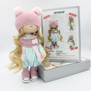 May include: DIY doll kit featuring a pink and blue doll wearing a pink hat and a scarf. The kit includes fabric, stuffing, and instructions. The box is silver with the text "DIY Doll Kit" and "Room Decor" printed on it.