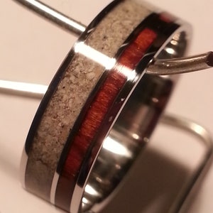 May include: A silver ring with a red and white inlay. The ring is 6 mm wide and is size UK O.