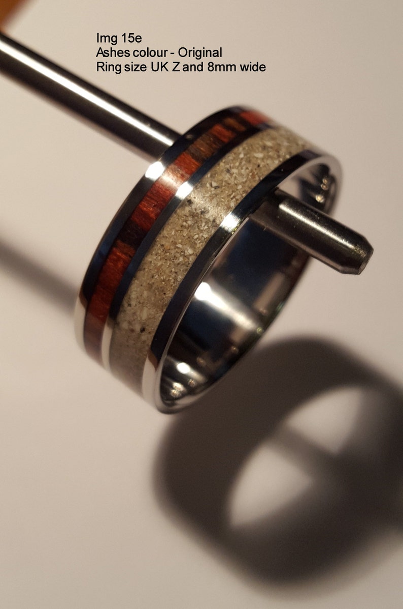 May include: A silver ring with a band of wood and white ash embedded in the metal. The ring is 8mm wide and is shown on a ring sizer.