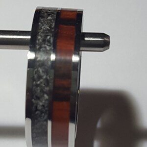 May include: A close-up of a silver ring with a black and red inlay. The ring is on a white surface.