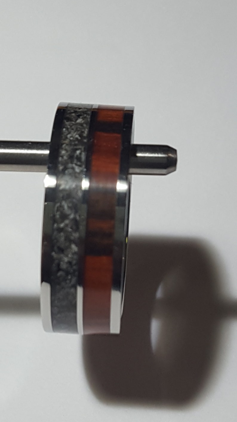 May include: A close-up of a silver ring with a black and red inlay. The ring is on a white surface.