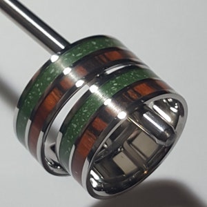 May include: Two rings with a silver band and green and brown wood inlay. The rings are stacked on top of each other.