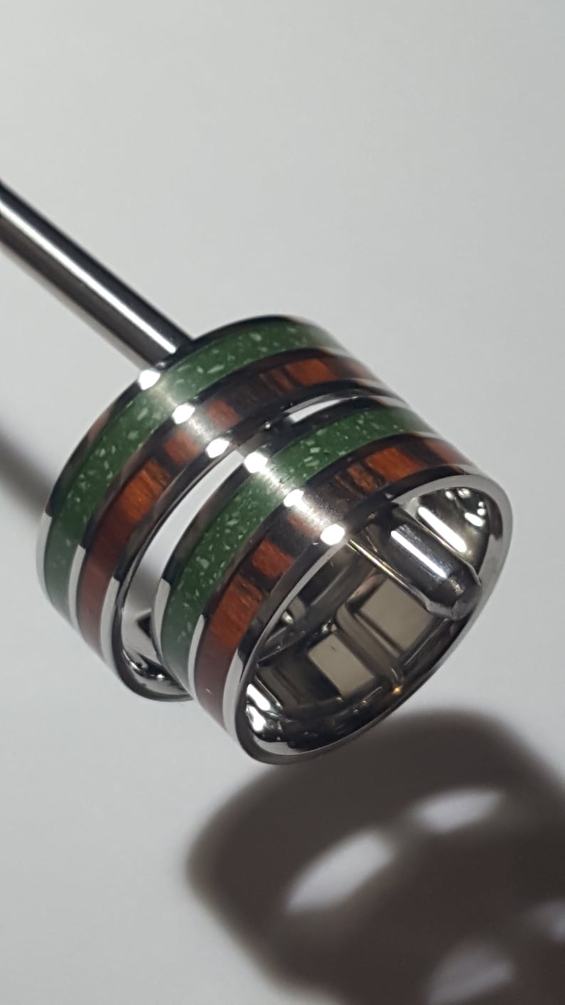 May include: Two rings with a silver band and green and brown wood inlay. The rings are stacked on top of each other.
