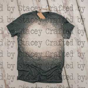 May include: A dark gray t-shirt with a white bleach splatter design. The shirt has a tag attached to the neck.