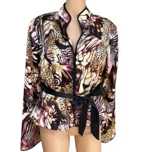 May include: A patterned jacket with a black tie belt. The jacket features a mix of animal print patterns in shades of brown, tan, and pink. It has a mandarin collar and a black trim. The jacket is a long-sleeved garment.