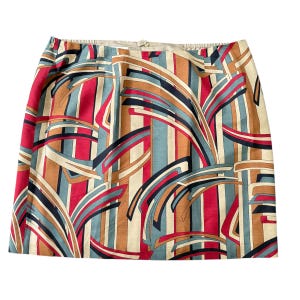 Peut inclure: Jupe trapèze avec un motif abstrait coloré. Le design présente des rayures verticales et des formes courbes en rouge, bleu, beige et noir. La jupe a une ceinture beige et une fermeture boutonnée.