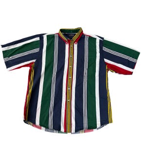 Pode incluir: Camisa de manga curta com botões e listras verticais em verde, branco, azul marinho, vermelho e amarelo. A camisa tem gola abotoada e um bolso no peito. As listras são espaçadas uniformemente.