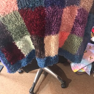 May include: A multi-colored fuzzy rug with a patchwork design in shades of blue, green, pink, red, and brown. The rug is draped over a chair with silver legs.
