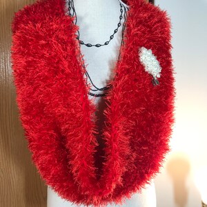 May include: A red fuzzy infinity scarf with a white pearl brooch.
