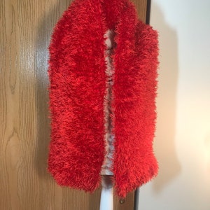 May include: A bright orange fuzzy scarf draped over a white mannequin. The scarf is made of a soft, fluffy material.