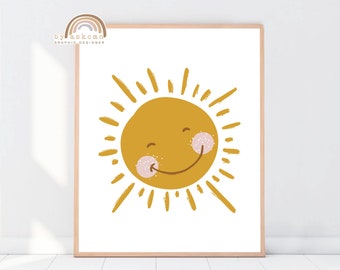 May include: A framed art print featuring a smiling sun illustration. The sun is a warm yellow color with a smiling face, pink cheeks, and radiating lines. The text "by askcmn GRAPHIC DESIGNER" is in the upper left corner.