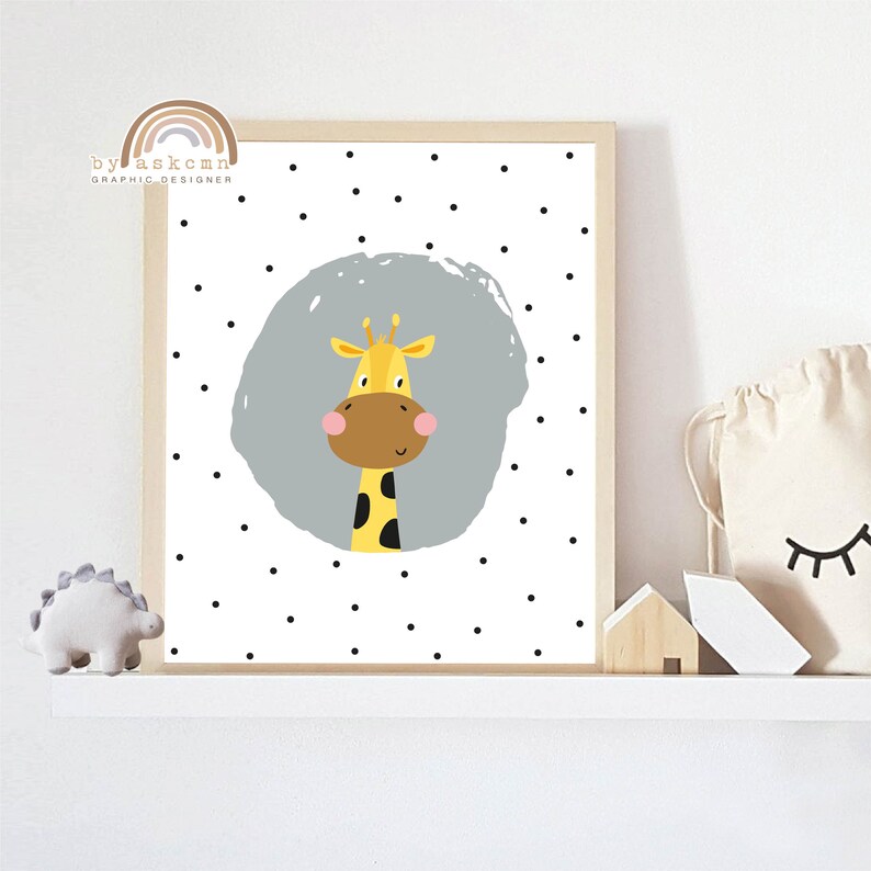 May include: A framed print featuring a cartoon giraffe with a yellow head, brown snout, and black spots on its neck. The giraffe is set against a gray circle on a white background with black polka dots. The print is in a light wood frame.
