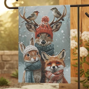 May include: A winter-themed garden flag featuring a deer, rabbit, and fox wearing scarves and hats. The background is a snowy scene with falling snowflakes.